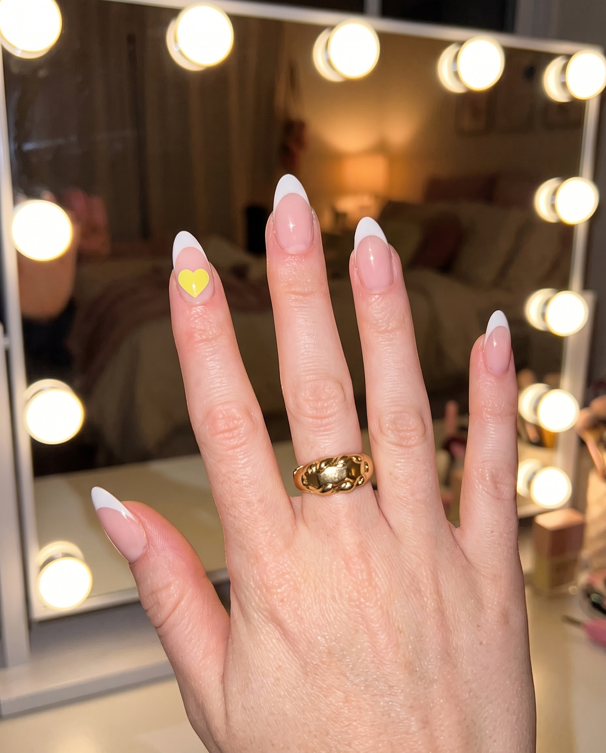 French-tip nails with a yellow Lumeria heart sticker in front of a vanity mirror