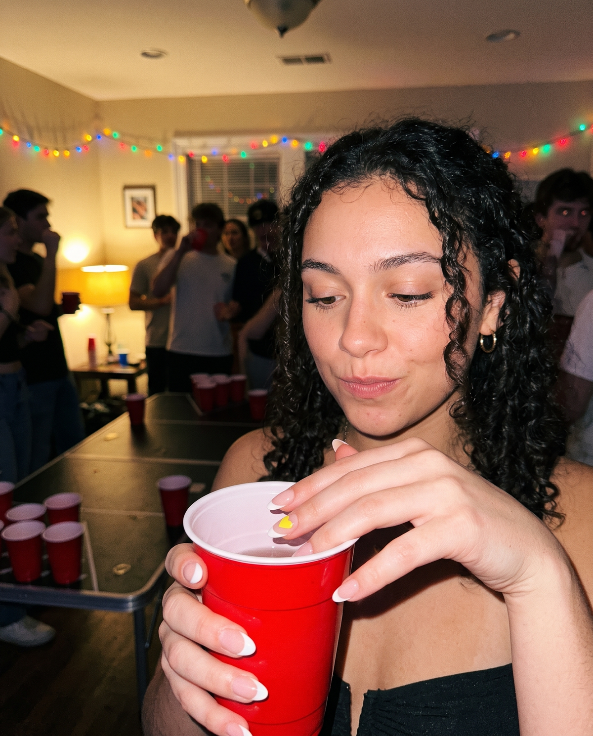 Girl at a college party dipping her Lumeria-stickered nail into her drink