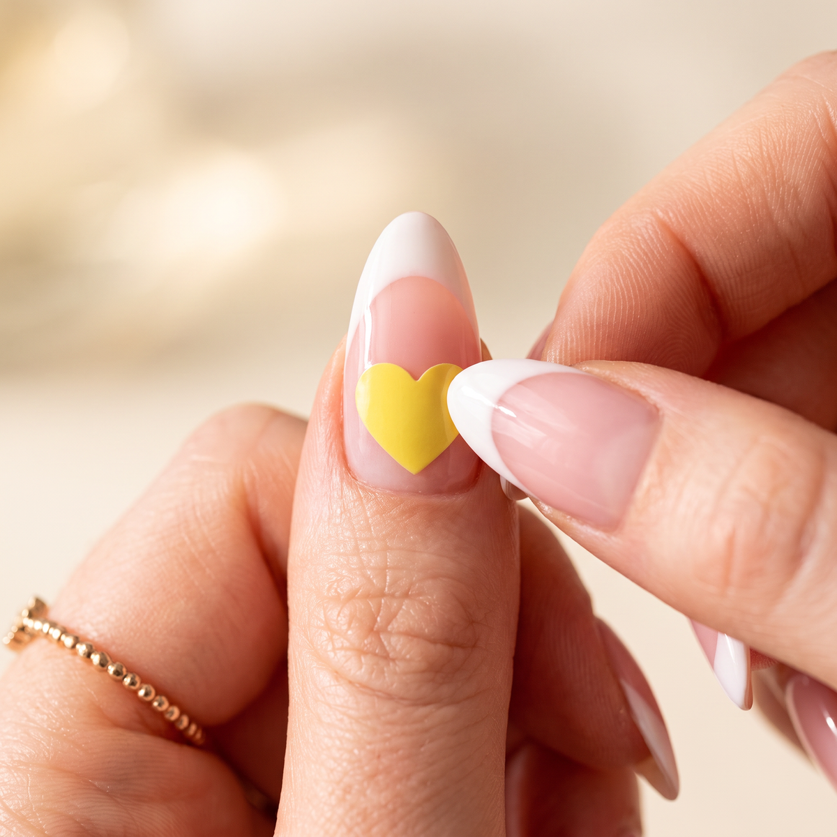 Pressing a yellow Lumeria heart sticker onto a pink French-tip nail