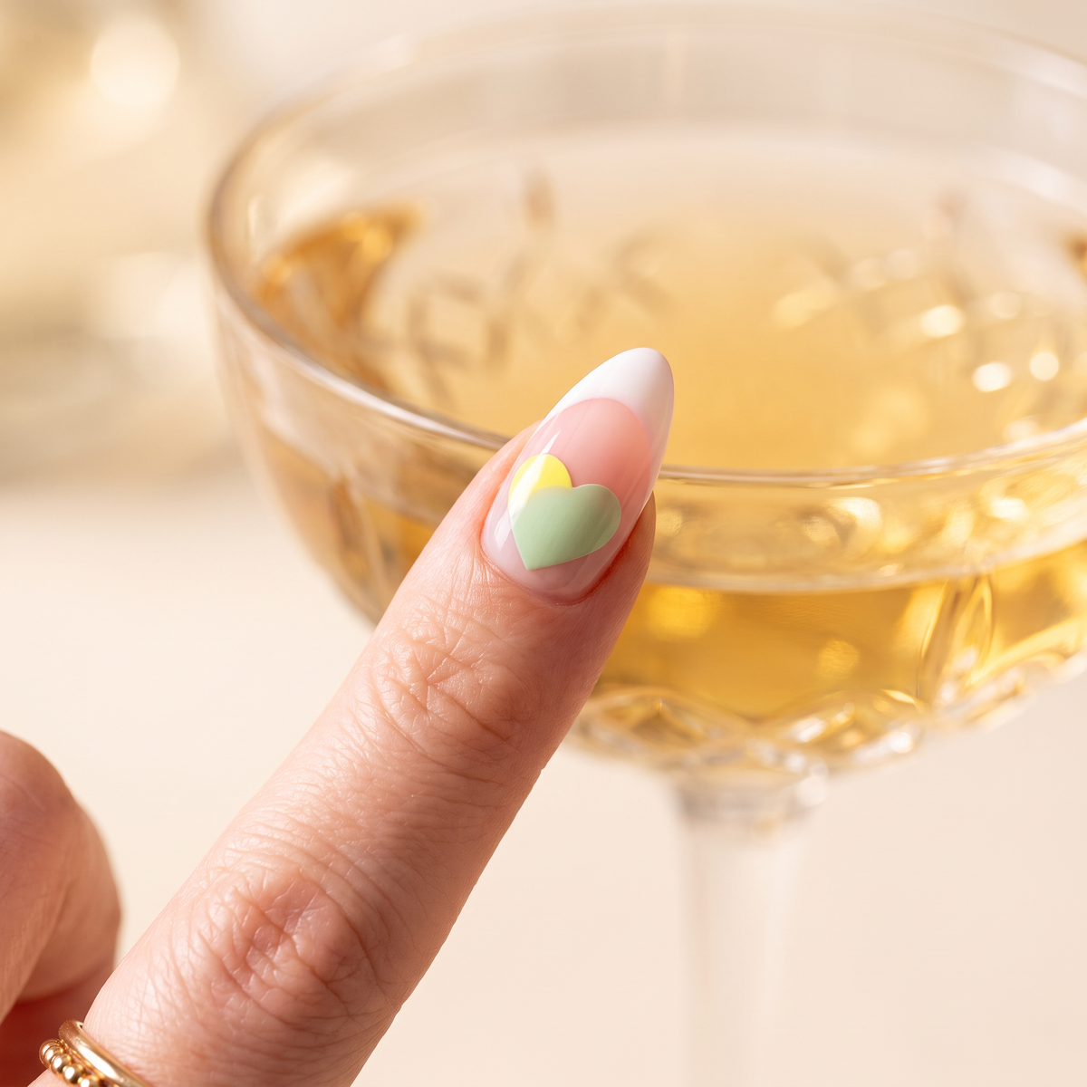 Yellow heart sticker on an index nail partly turned soft green in front of a cocktail